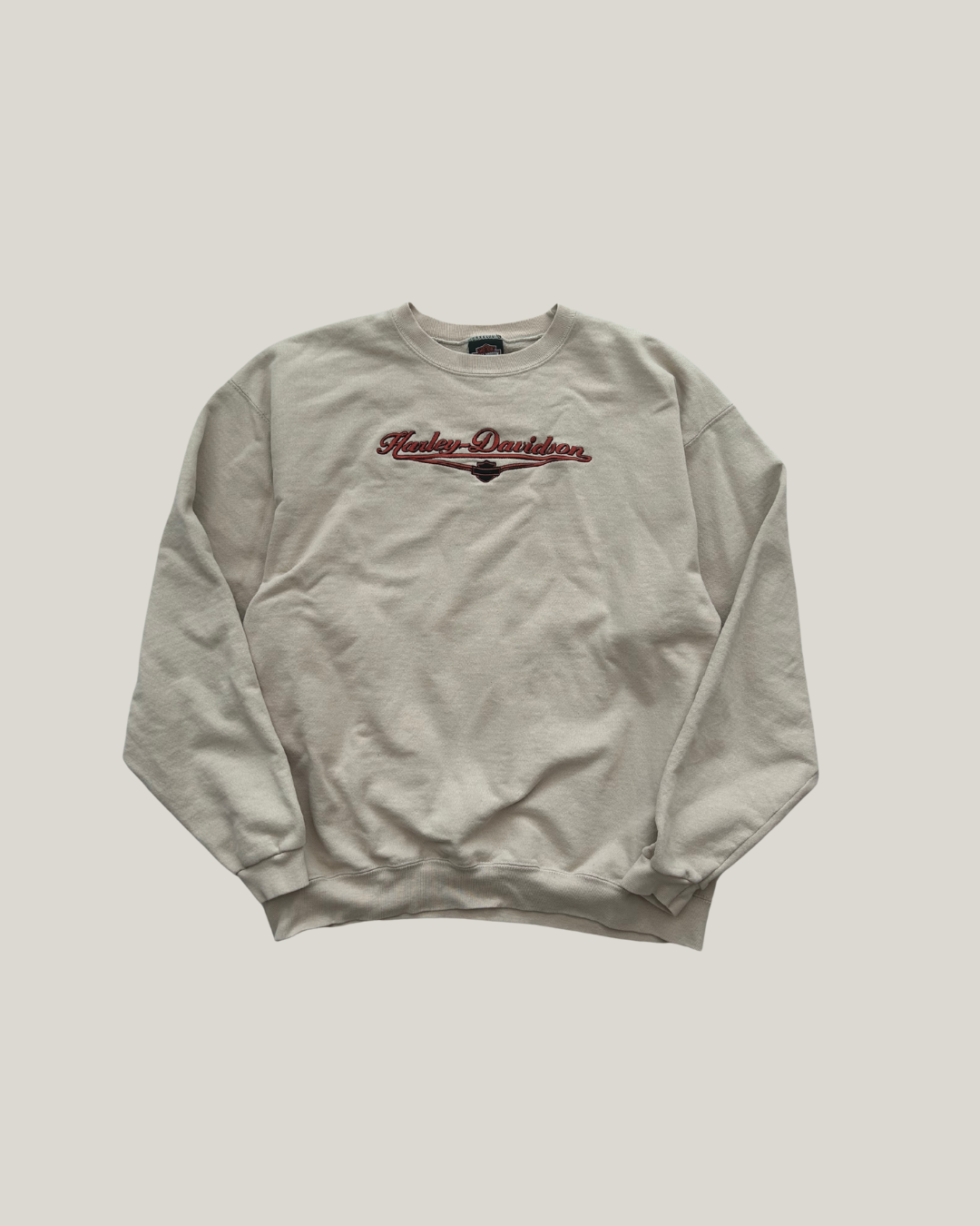 Beige Harley-Davidson sweatshirt with red and black text on a chest on a light gray background