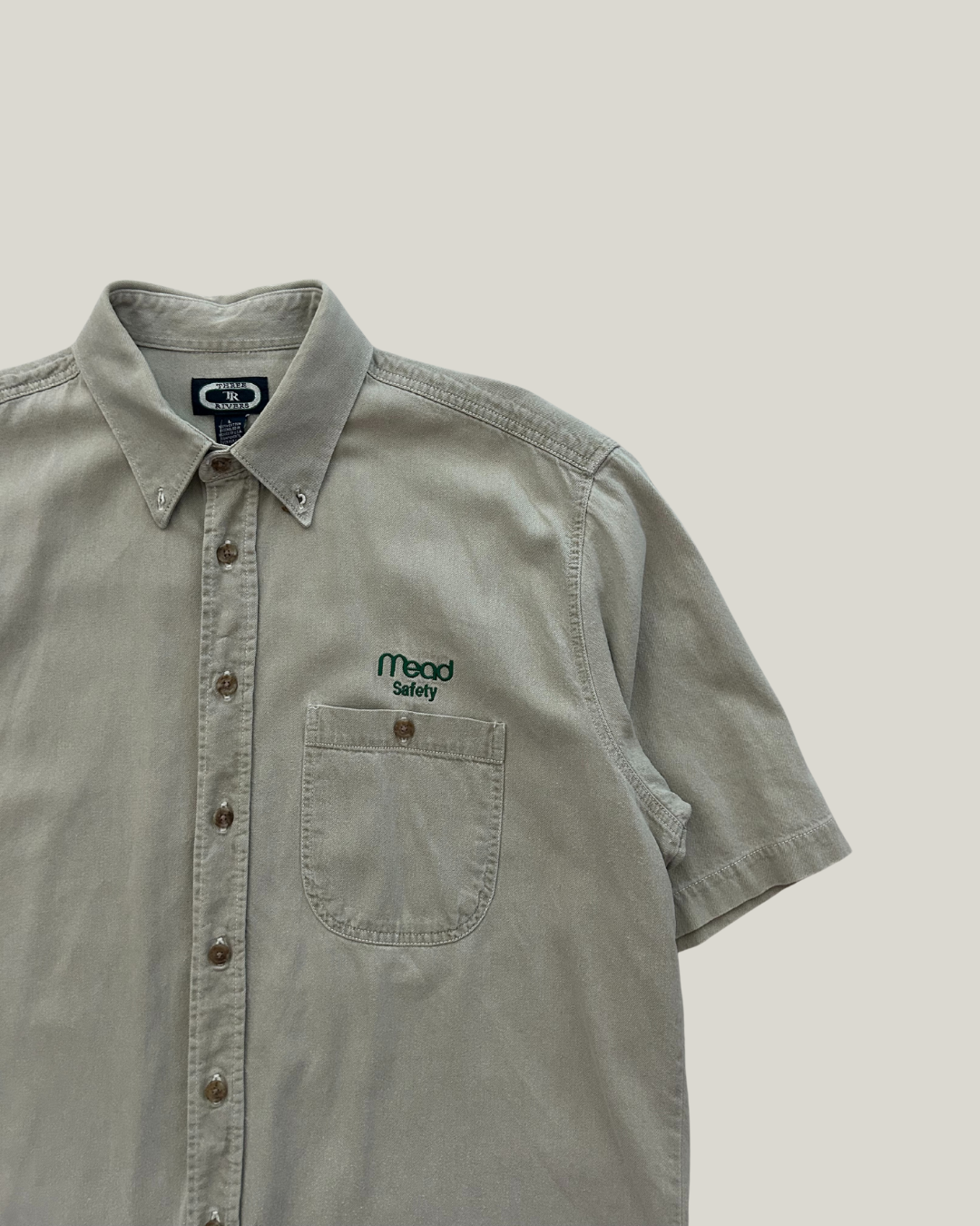 beige short-sleeve shirt with a "mead safety" logo on a beige background