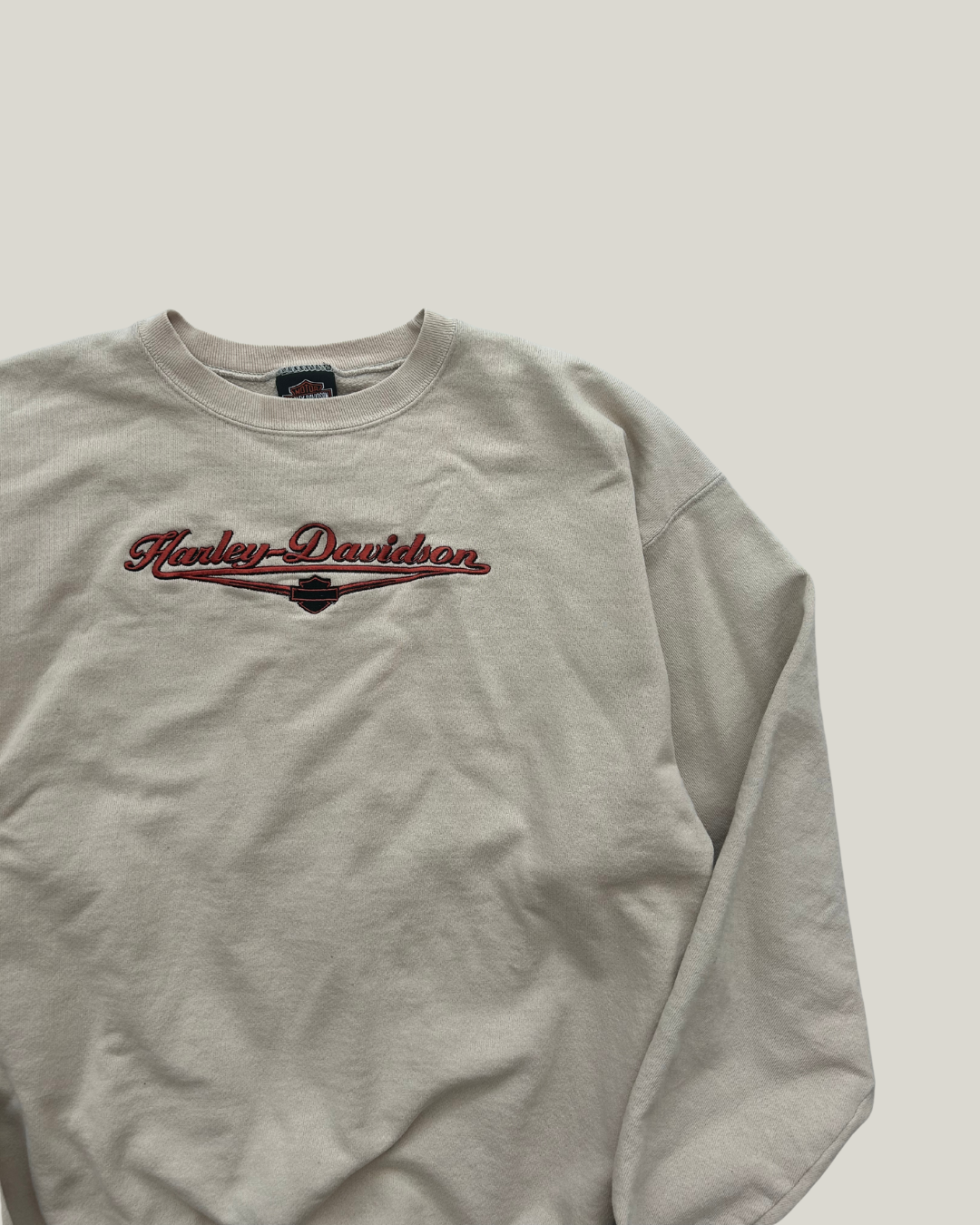Beige sweatshirt with red 'Harley Davidson' logo on a chest on light gray background