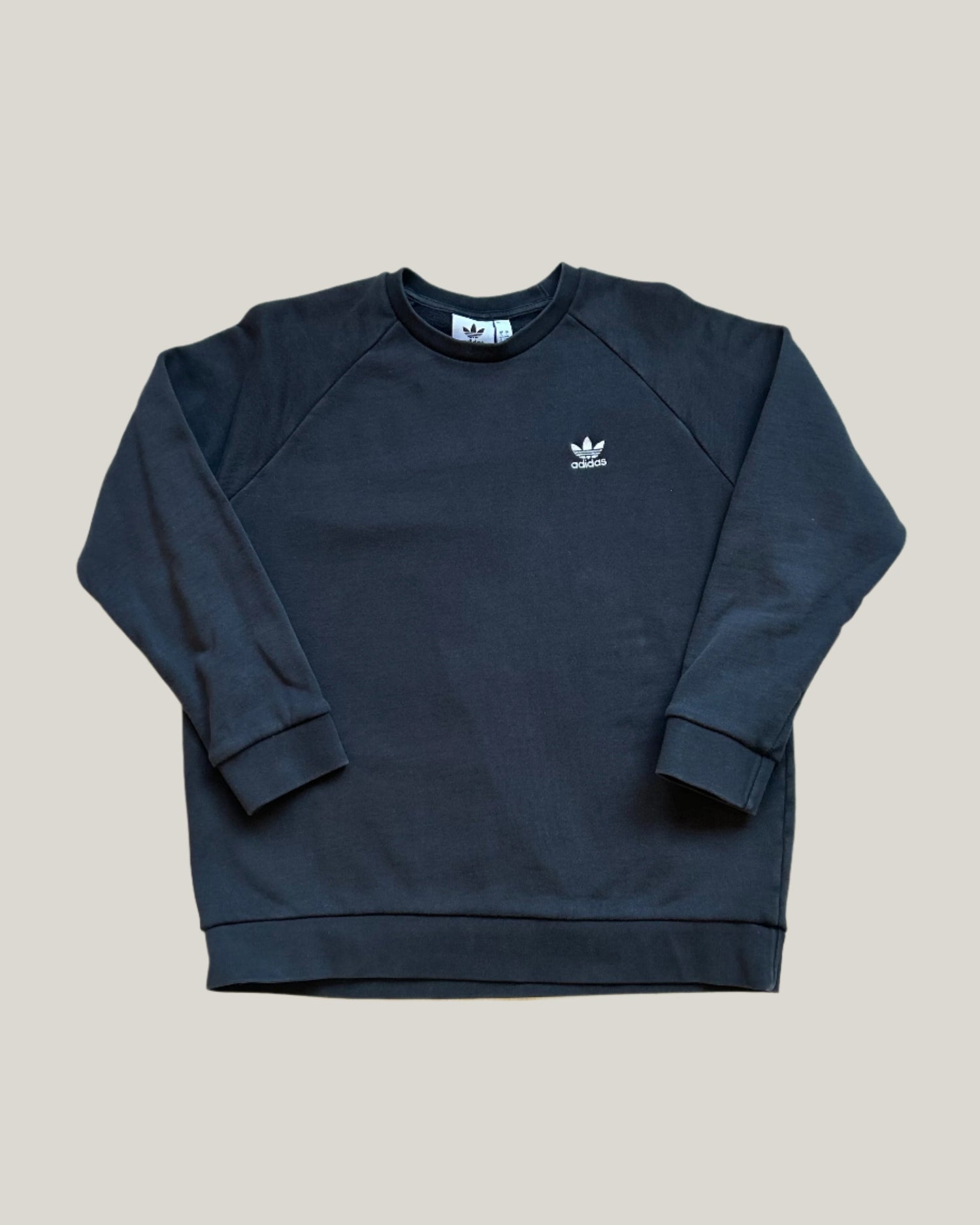 This image features a stylish, black Adidas crewneck sweatshirt, characterized by its comfortable fit and minimalist design. The sweatshirt prominently displays the Adidas signature trefoil logo in white on the chest, serving as a distinctive brand marker.